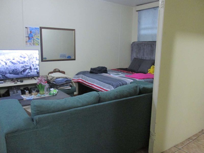 An open-plan living and bedroom area featuring tiled flooring and a window, providing a functional layout for apartment living.