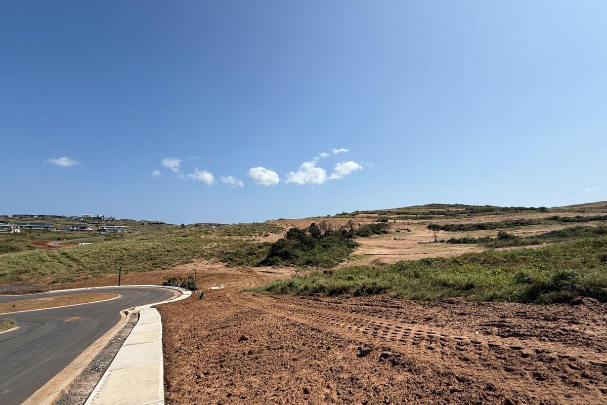 A view of a vacant residential plot featuring a paved road and concrete curbing, ready for development in a coastal estate setting.