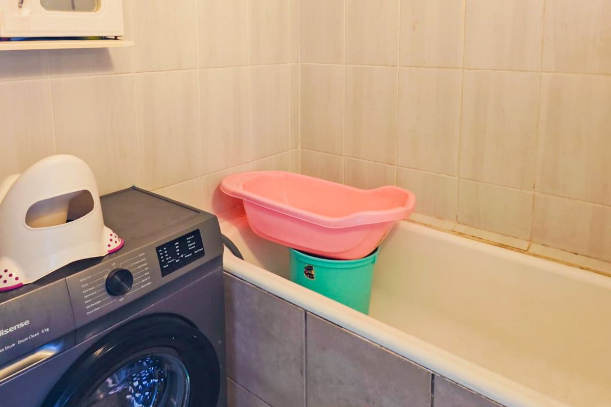 A functional bathroom featuring a standard bathtub and tiled walls, currently utilized as a laundry area with a washing machine.