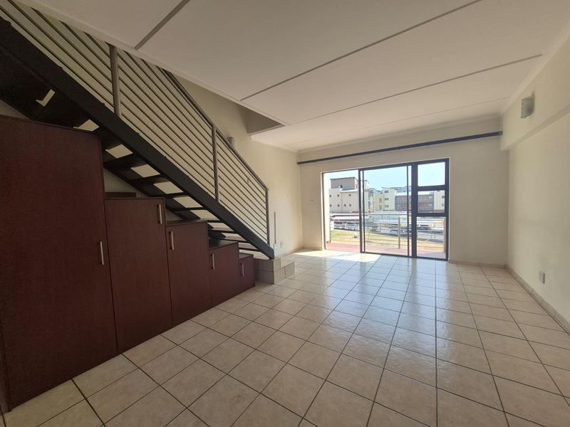 Spacious open-plan living area featuring tiled flooring, a staircase with integrated under-stair storage, and large sliding glass doors leading to an outdoor space.