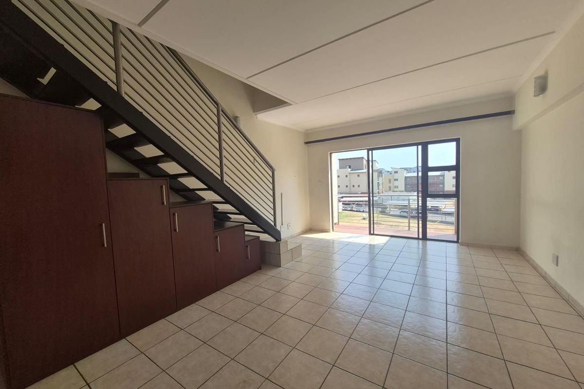 Spacious open-plan living area featuring tiled flooring, a staircase with integrated under-stair storage, and large sliding glass doors leading to an outdoor space.