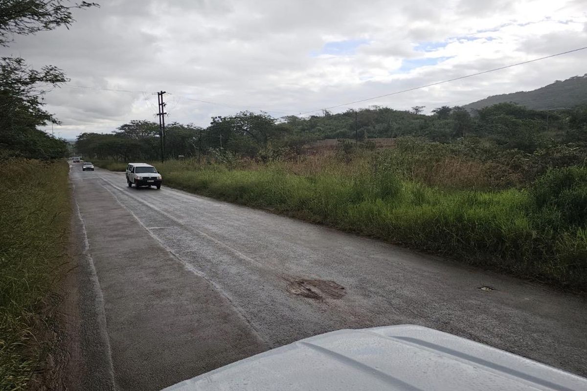 A view of the asphalt access road leading to the property, featuring overhead power lines and visible road surface wear.