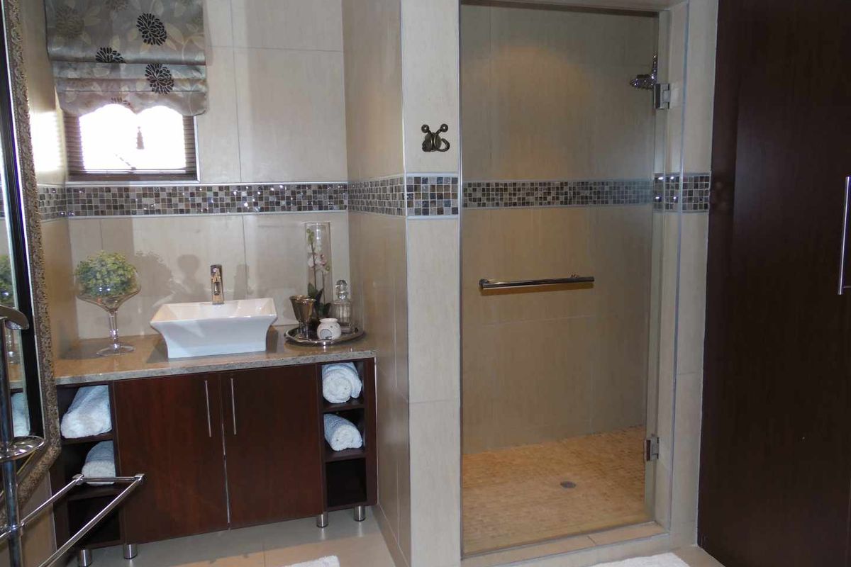 A modern bathroom featuring a vessel sink vanity with dark wood cabinetry, a glass-enclosed walk-in shower, and neutral wall tiling with mosaic accents.
