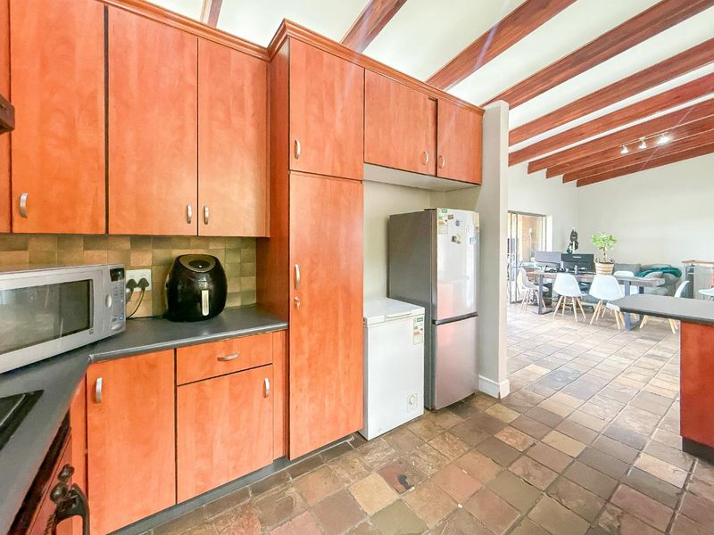 Open-plan kitchen featuring wooden ceiling beams, tiled flooring, and ample built-in cabinetry, flowing seamlessly into the adjacent dining and living area.