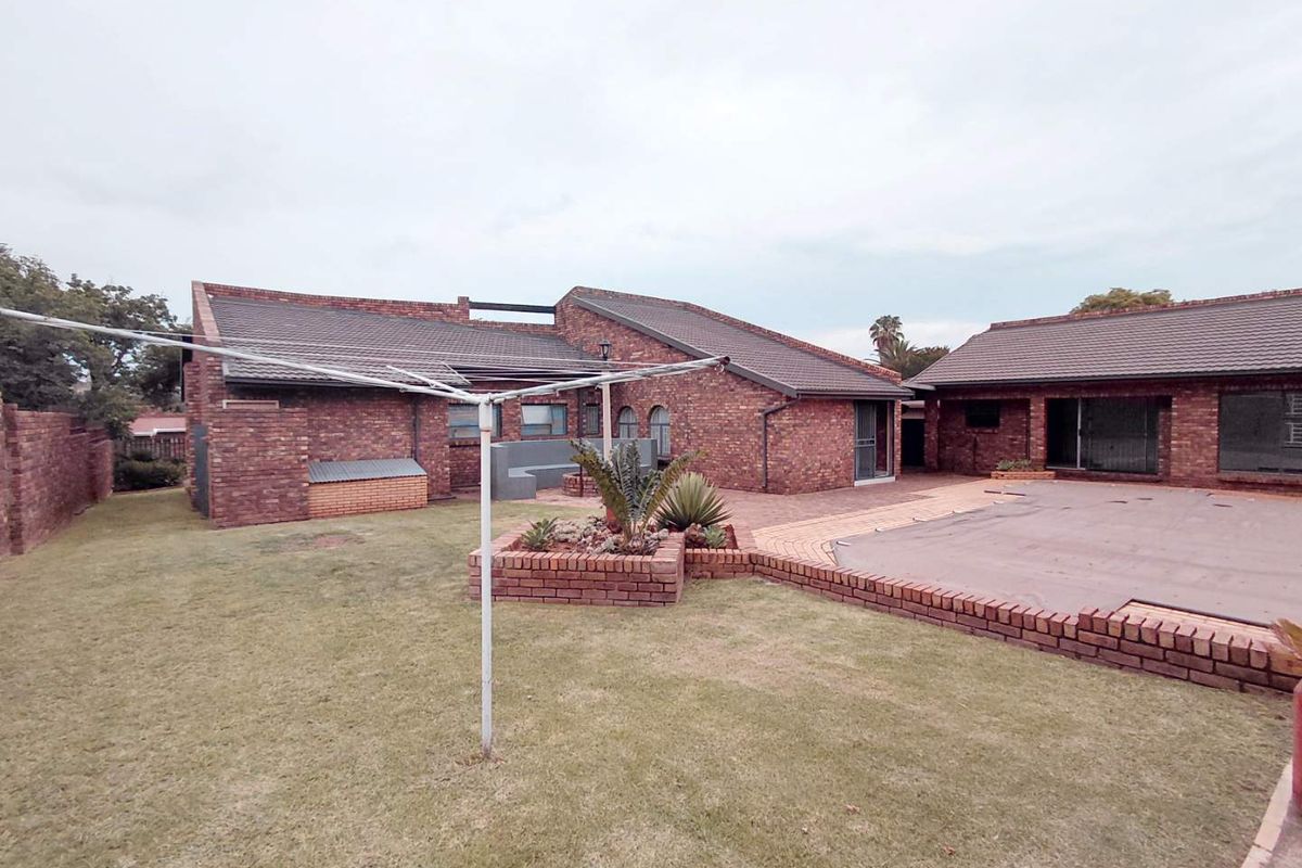 Rear view of the property featuring a brick facade, tiled roof, paved patio area, and a swimming pool with a cover.