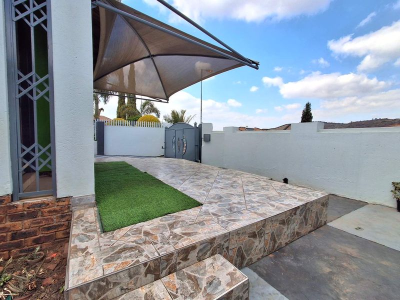 A paved outdoor patio area featuring a shade sail, boundary wall, and secure metal gate access.
