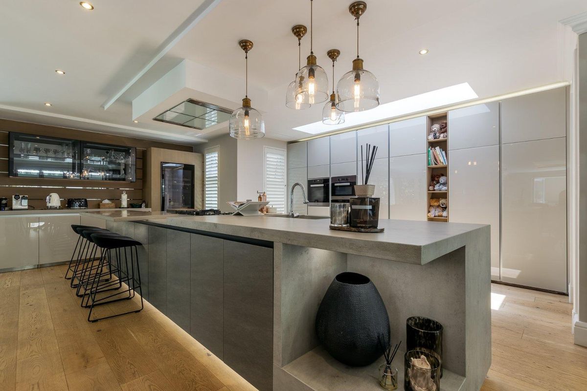 Modern open-plan kitchen featuring a large concrete-style island, integrated appliances, sleek cabinetry, and stylish pendant lighting with timber flooring.