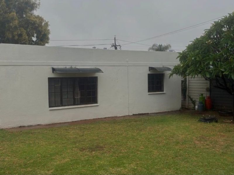 A view of the rear exterior elevation of the house, featuring a simple facade with window awnings and a surrounding lawn area.