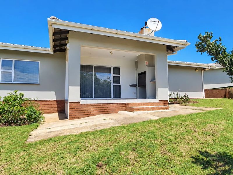 Rear view of the property featuring a covered patio with a built-in braai, sliding glass doors, and a spacious garden area.