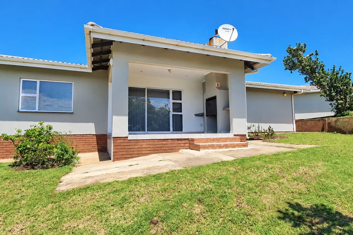 Rear view of the property featuring a covered patio with a built-in braai, sliding glass doors, and a spacious garden area.