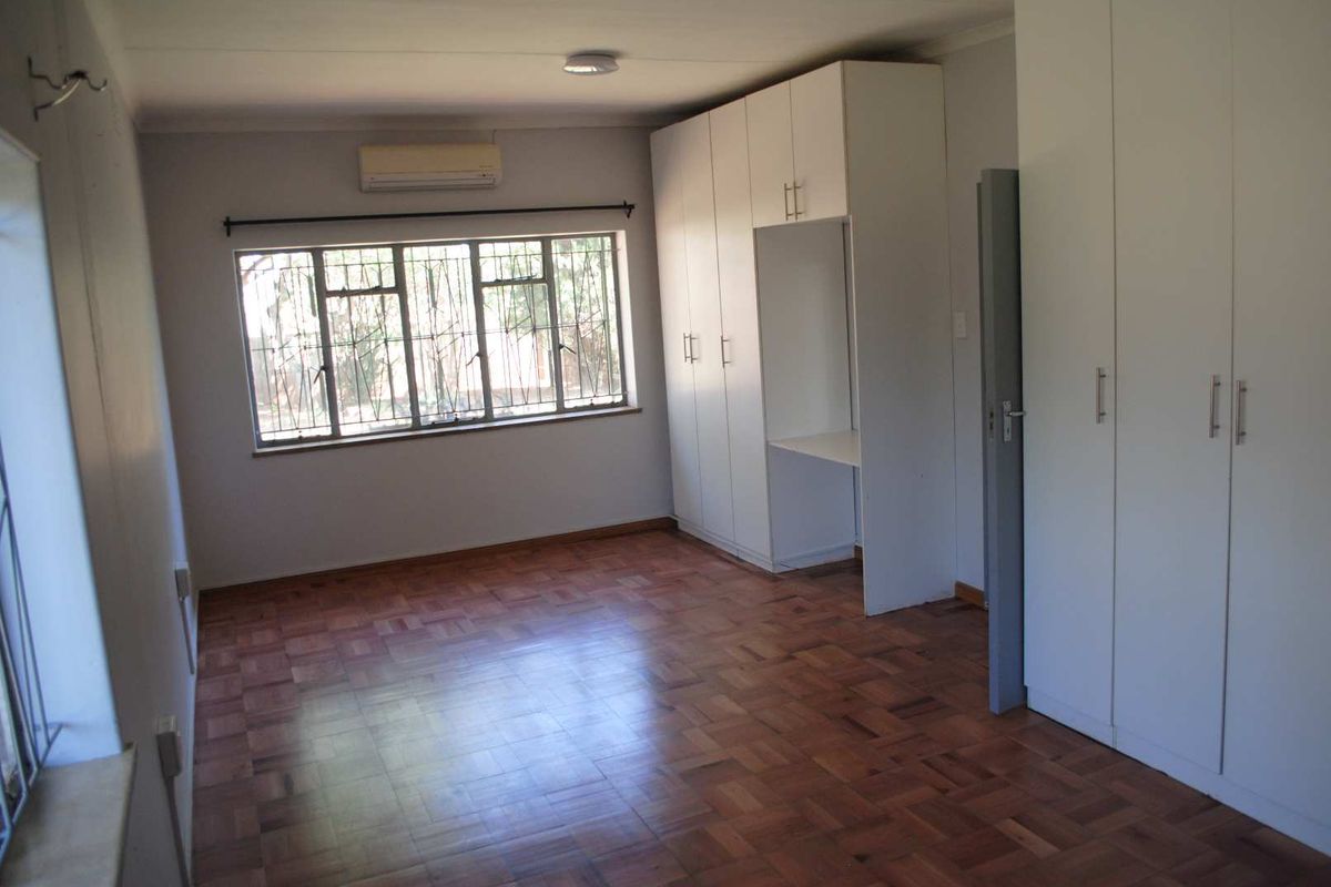 A bright bedroom featuring polished parquet flooring, extensive built-in cabinetry, and a wall-mounted air conditioning unit.