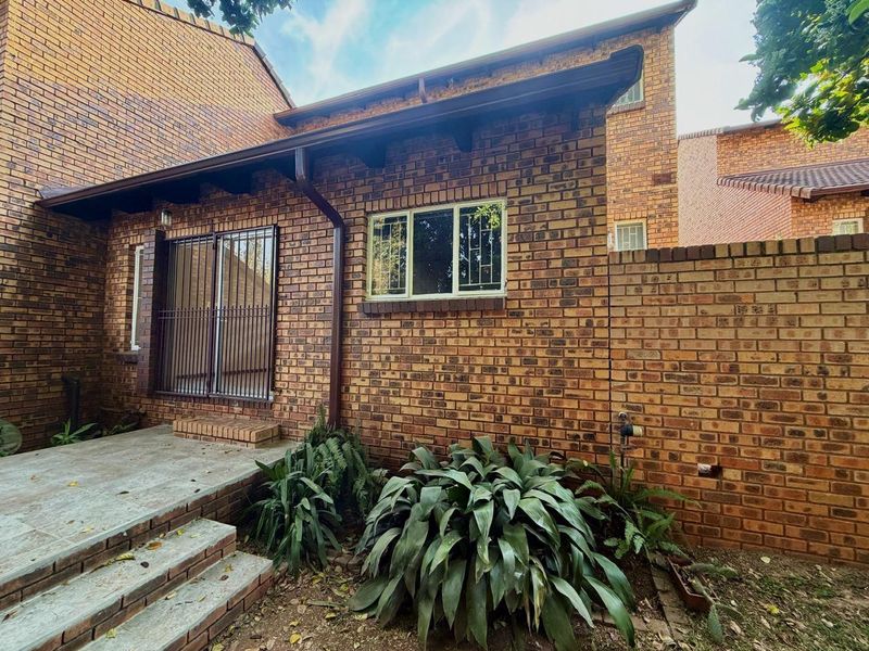 Rear exterior view of the townhouse featuring face brick construction, a small concrete patio, and secure metal window and door grilles.
