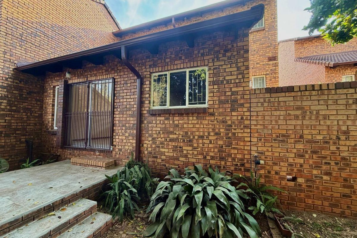 Rear exterior view of the townhouse featuring face brick construction, a small concrete patio, and secure metal window and door grilles.