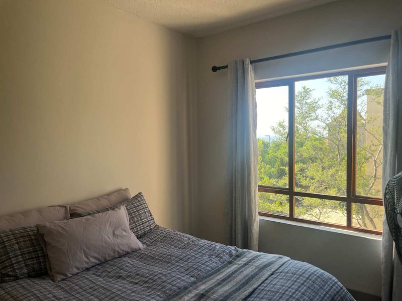 A cozy bedroom featuring a large window that provides natural light and a pleasant view of the surrounding greenery.