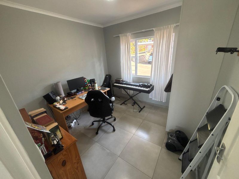 A functional home office space featuring neutral wall tones, tiled flooring, and a window providing natural light.