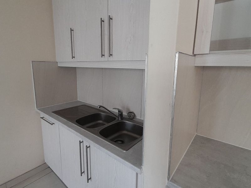 A clean and functional scullery area featuring built-in cabinetry, a stainless steel double sink, and tiled splashbacks.