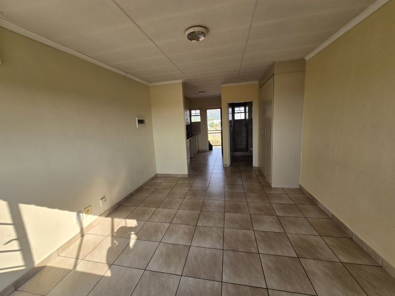 An empty open-plan living area featuring tiled flooring, built-in storage cupboards, and neutral wall finishes, providing a blank canvas for interior design.