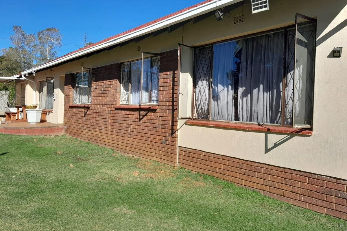 Rear exterior view of the house featuring a brick and plaster facade, metal security window bars, and a well-maintained lawn area.