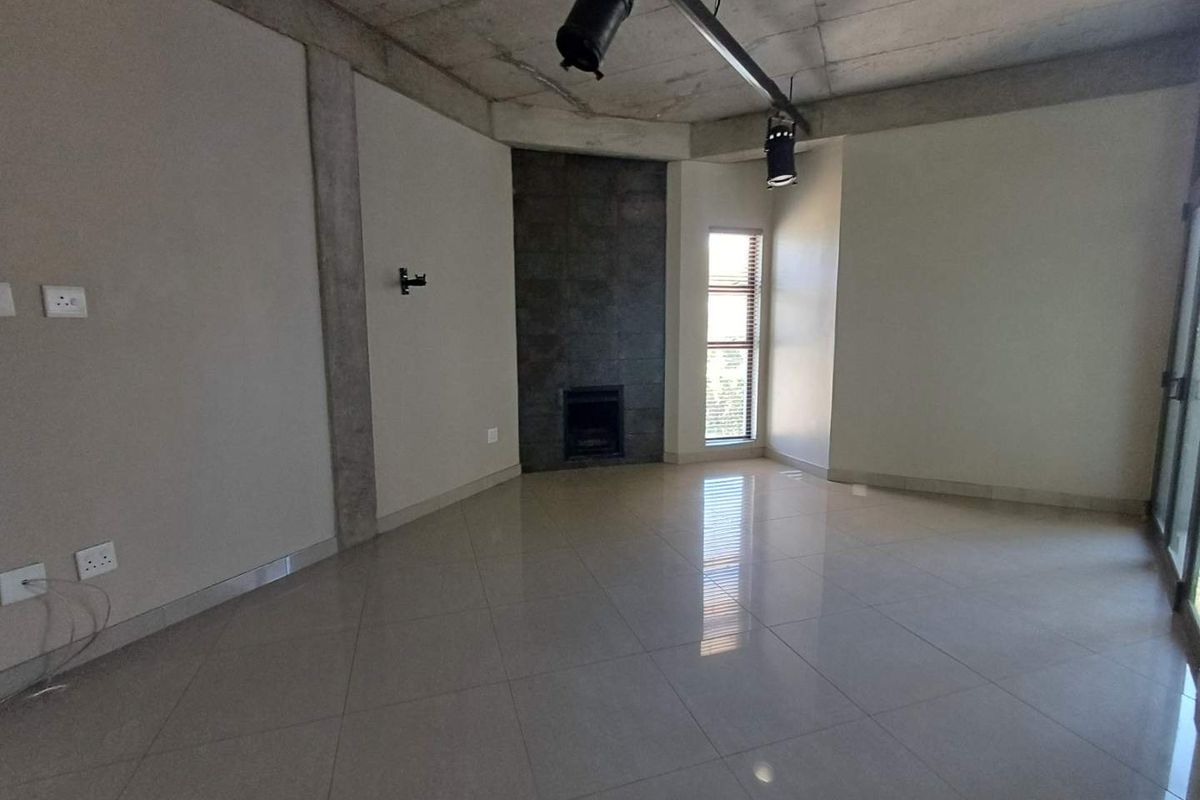 Spacious living area featuring polished tile flooring, an exposed concrete ceiling with track lighting, and a built-in fireplace with stone cladding.