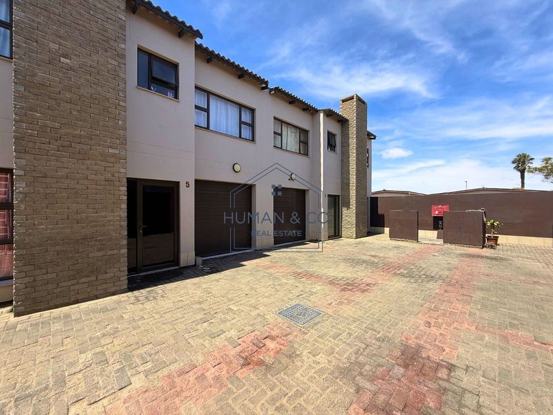 Front elevation of a townhouse featuring a paved driveway, double garage, and brick facade detailing.