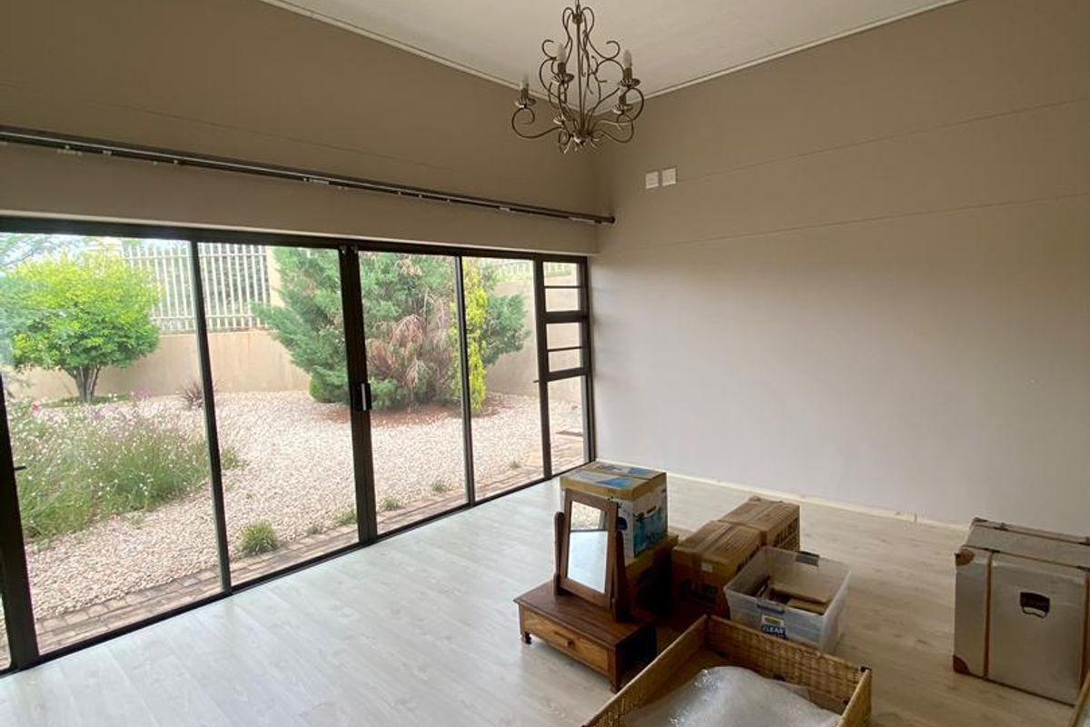 Spacious living area featuring light wood-look flooring, a decorative chandelier, and large sliding glass doors providing direct access to the rear garden.