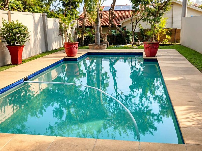 A well-maintained rectangular swimming pool featuring a tiled surround, bordered by a lawn and high boundary walls for privacy.