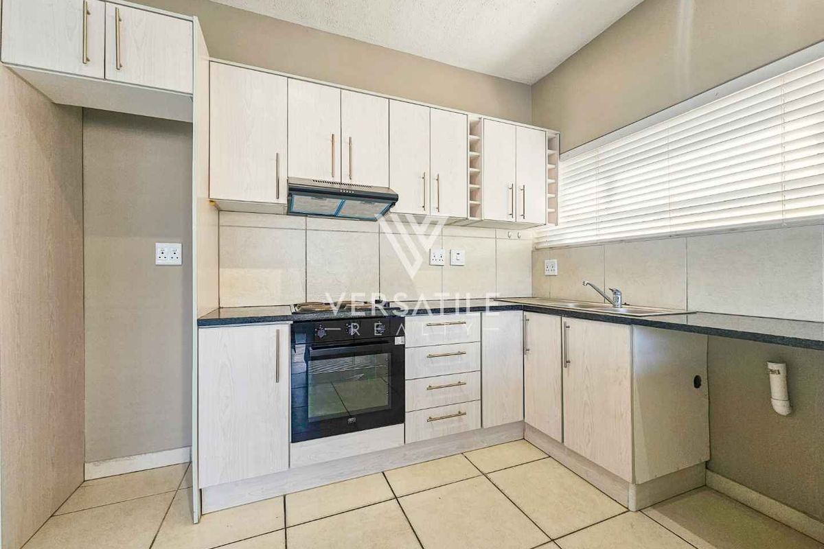 A clean, functional kitchen featuring light-toned cabinetry, built-in oven with extractor fan, tiled backsplash, and ample counter space with a stainless steel sink.