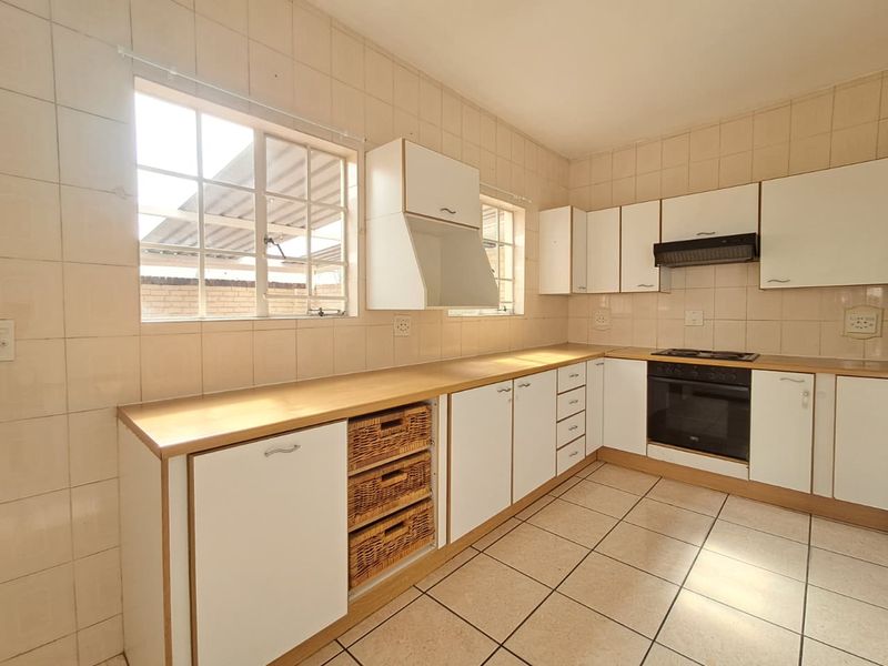 A functional kitchen featuring white cabinetry, laminate countertops, built-in oven and hob, and full-height wall tiling with ceramic floor tiles.