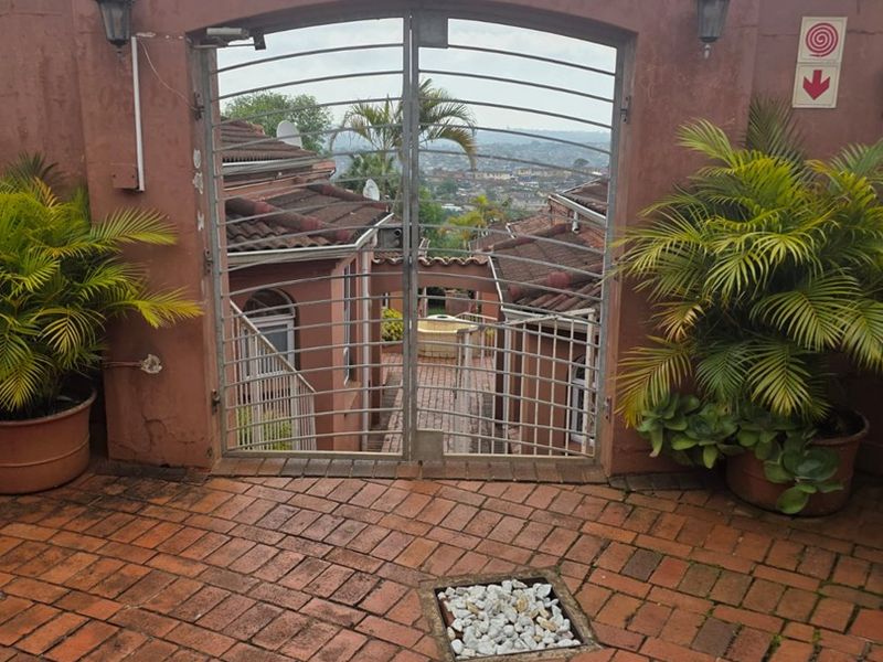 A paved outdoor patio area featuring a decorative metal security gate, wall-mounted lighting, and a view overlooking the surrounding townhouse complex.