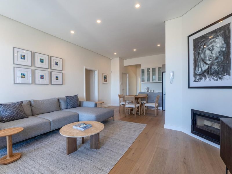 A bright open-plan living area featuring hardwood flooring, a built-in fireplace, and a seamless transition to a compact kitchen space.