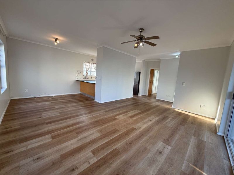 Spacious open-plan living area featuring modern laminate flooring, a ceiling fan, and a functional kitchen layout with built-in cabinetry.