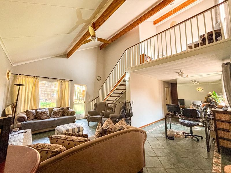 Spacious open-plan living area featuring vaulted ceilings with exposed timber beams, a mezzanine level, and tiled flooring throughout.