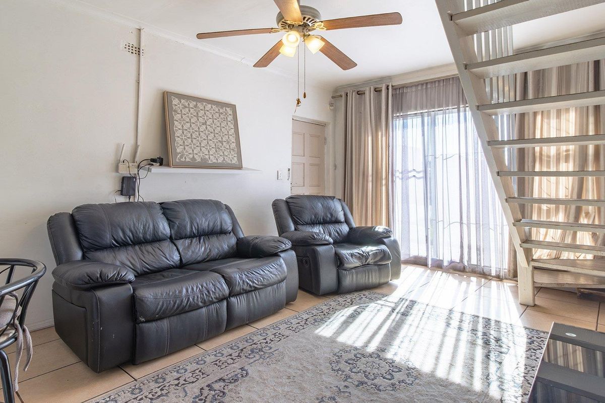 A living room featuring tiled flooring, a ceiling fan, and a staircase leading to the upper level, with access to an outdoor area.