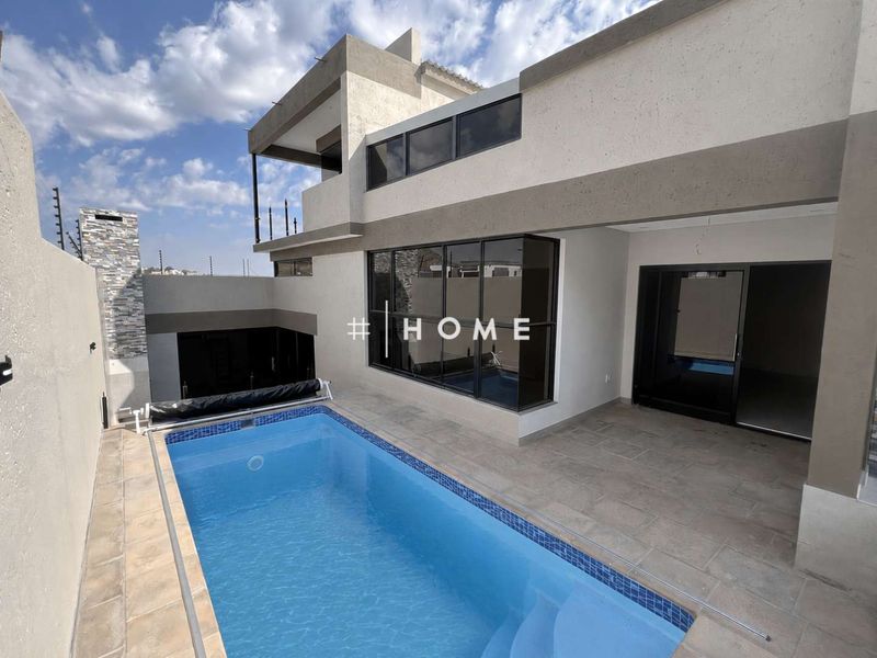 Modern double-story home exterior featuring a swimming pool, tiled patio area, and contemporary architectural finishes with large glass sliding doors.