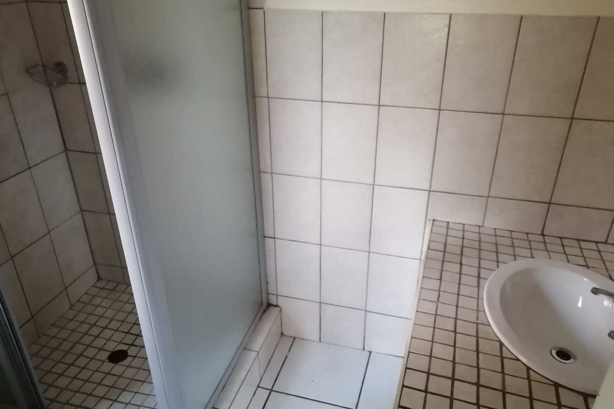 A functional bathroom featuring a shower enclosure, a tiled vanity countertop with a drop-in basin, and neutral ceramic wall and floor tiling.