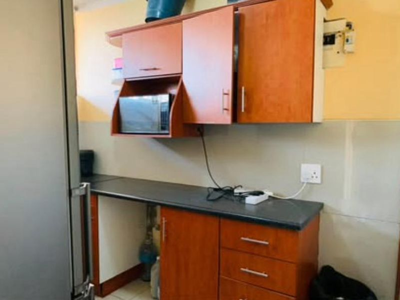 A compact kitchen area featuring wood-look cabinetry, dark laminate countertops, and a built-in microwave, requiring minor cosmetic updates to improve functionality and aesthetic appeal.
