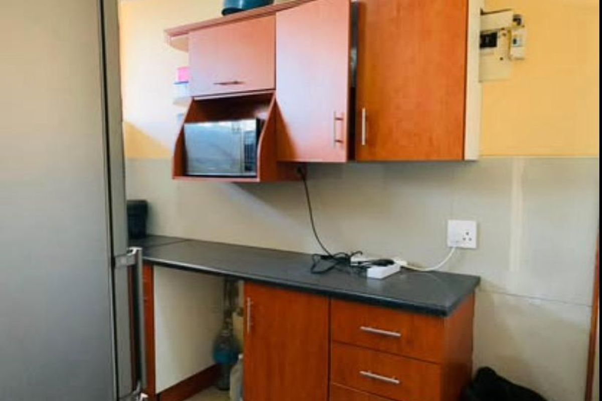A compact kitchen area featuring wood-look cabinetry, dark laminate countertops, and a built-in microwave, requiring minor cosmetic updates to improve functionality and aesthetic appeal.