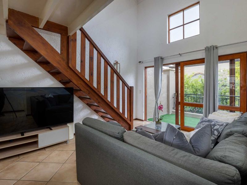 A double-volume living room featuring a wooden staircase, tiled flooring, and large glass sliding doors leading to an outdoor balcony area.