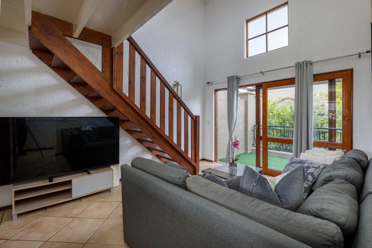 A double-volume living room featuring a wooden staircase, tiled flooring, and large glass sliding doors leading to an outdoor balcony area.