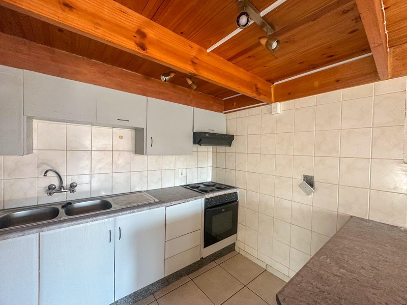 A functional kitchen featuring built-in cabinetry, a double sink, electric oven and hob, tiled splashbacks, and exposed timber ceiling beams.