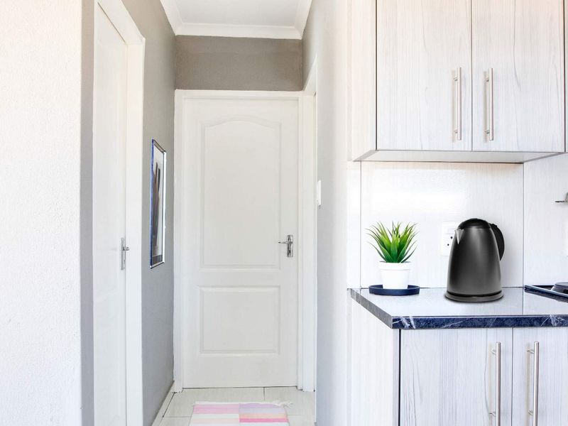 A functional kitchen area featuring built-in cabinetry, laminate countertops, and integrated cooking appliances, leading into a hallway with white panel doors.