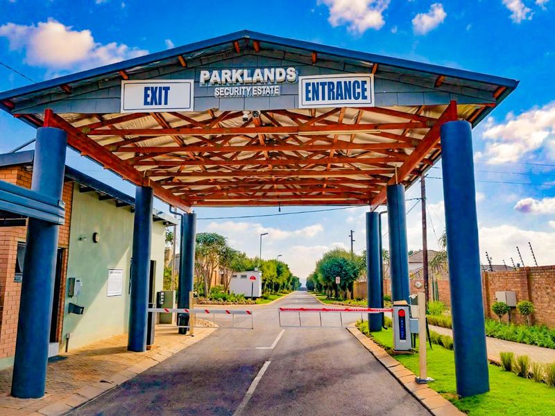 The main entrance and security gatehouse of Parklands Security Estate, featuring a paved driveway, boom gate access, and well-maintained perimeter walling.