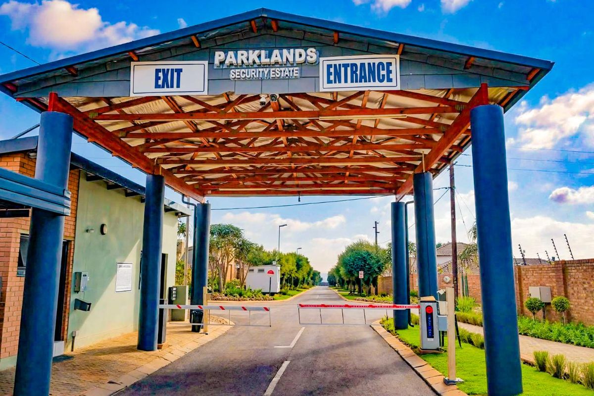 The main entrance and security gatehouse of Parklands Security Estate, featuring a paved driveway, boom gate access, and well-maintained perimeter walling.
