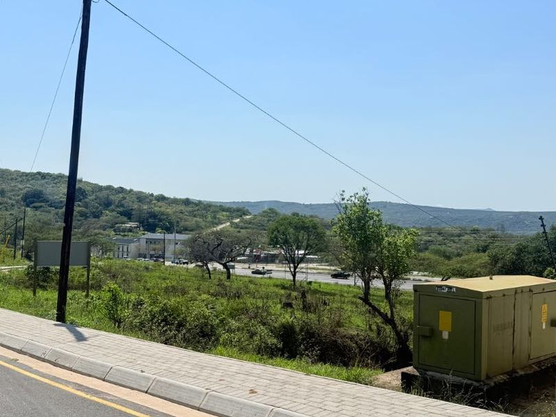 Street view of the vacant residential land showing the paved sidewalk, utility pole, and electrical transformer box with surrounding landscape.
