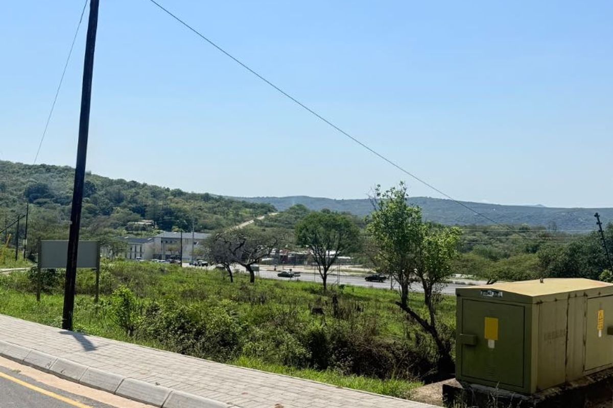 Street view of the vacant residential land showing the paved sidewalk, utility pole, and electrical transformer box with surrounding landscape.