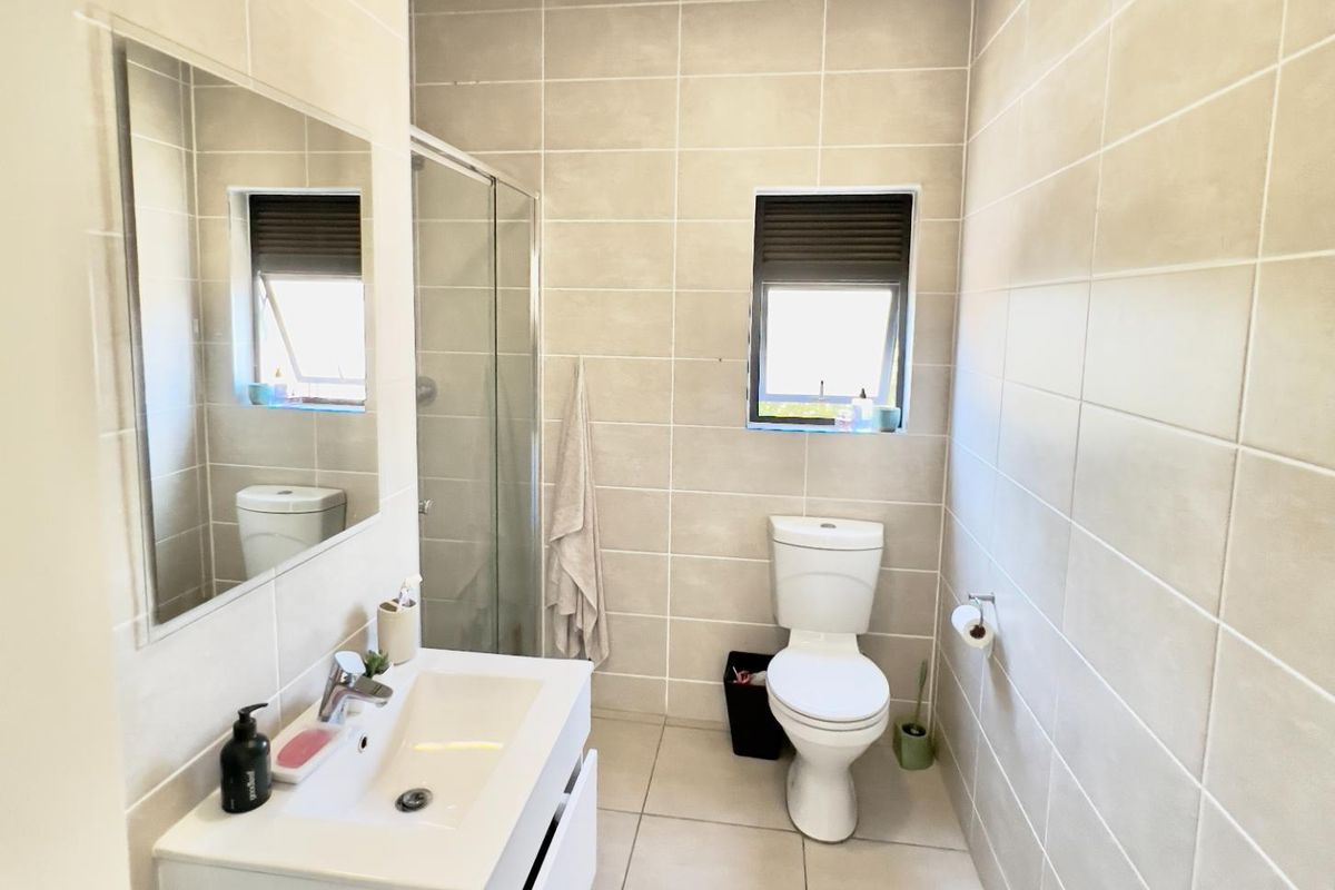 A modern bathroom featuring floor-to-ceiling neutral tiling, a glass-enclosed shower, a wall-mounted vanity with basin, and a toilet.