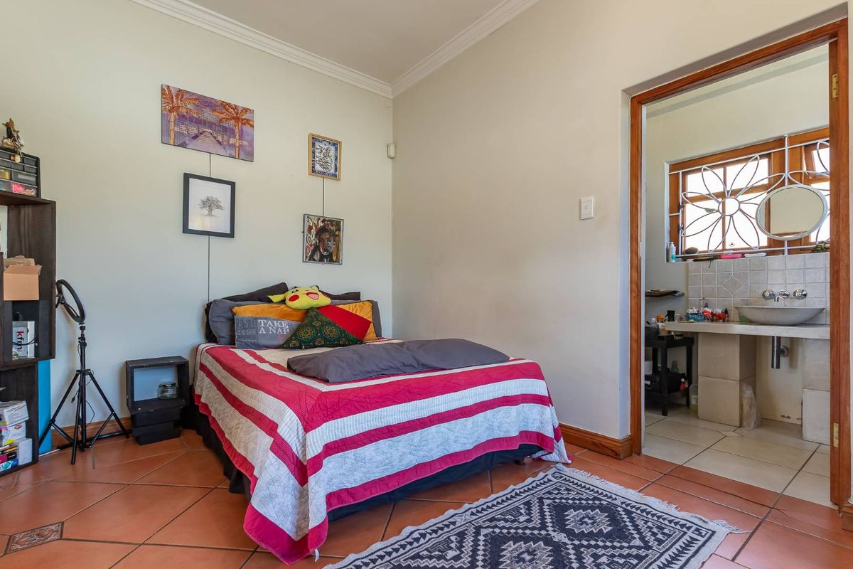 A bedroom featuring terracotta floor tiles and an en-suite bathroom with a basin and decorative window security gate.