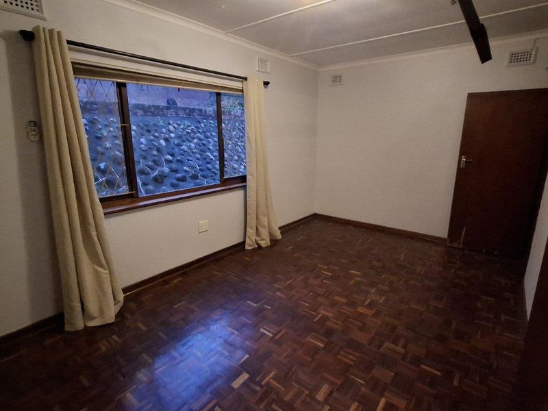 An empty bedroom featuring classic parquet flooring, neutral walls, and a window with security bars, offering a blank canvas for personalization.