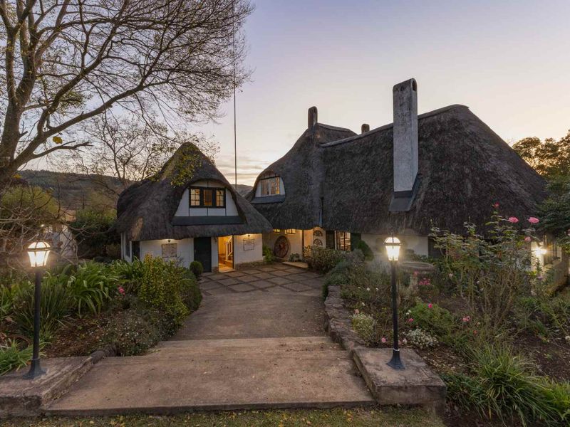 Charming guest house exterior featuring a traditional thatched roof, stone chimney, and a welcoming paved entrance path surrounded by landscaped gardens.