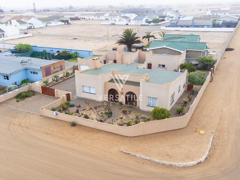 Aerial view of a single-story residential property featuring a perimeter wall, driveway, and metal roofing in a coastal neighborhood setting.